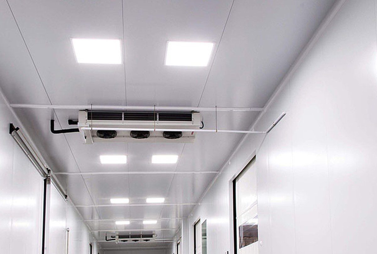 Pasillo de sala blanca con panel sanitario, iluminación estanca y evaporadores