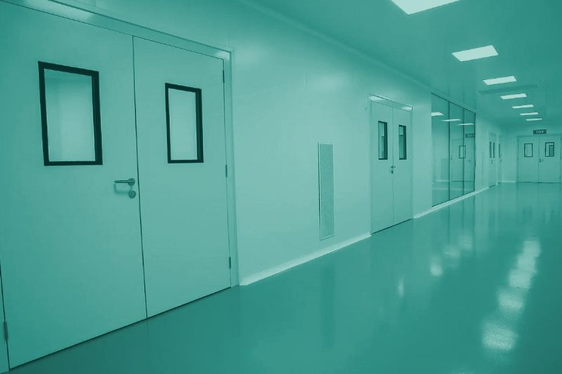 Pasillo de sala blanca con puertas y suelo técnico